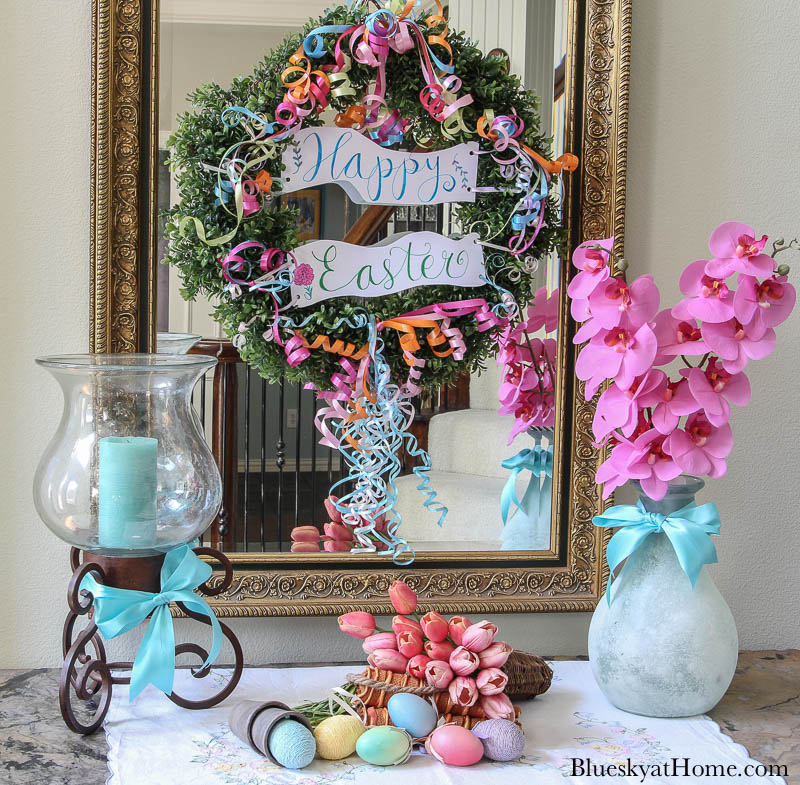 light blue vase with pink orchids, candle holder with aqua candle, Easter wreath on mirror