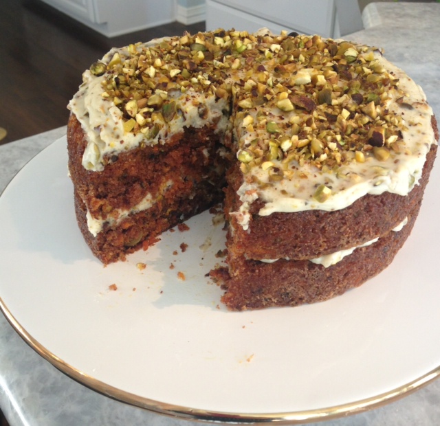 A plate holding a Pistachio Carrot Cake, revealing a missing slice that highlights its moist texture and carrot-filled goodness.