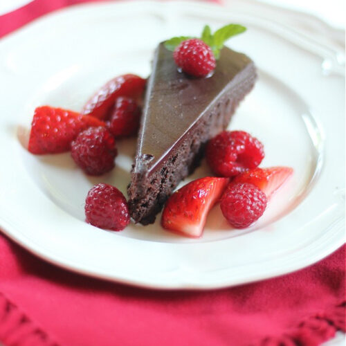 slice of Chocolate Cassis cake with strawberries and raspberries on a white plate