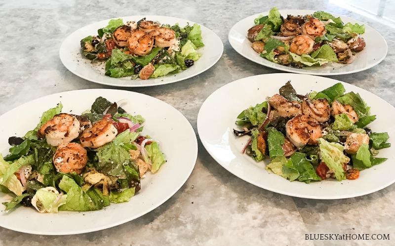  4 green salads with shrimp on white plates