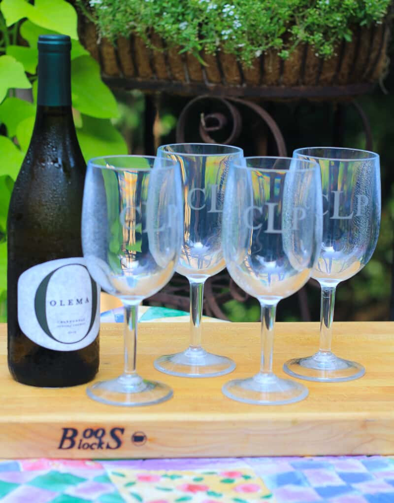 set of wine glasses on large cutting board with wine bottle outdoors for summer picnic