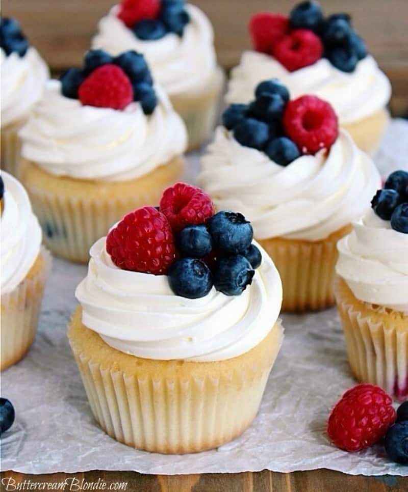 white cupcakes with raspberries and blueberries on top