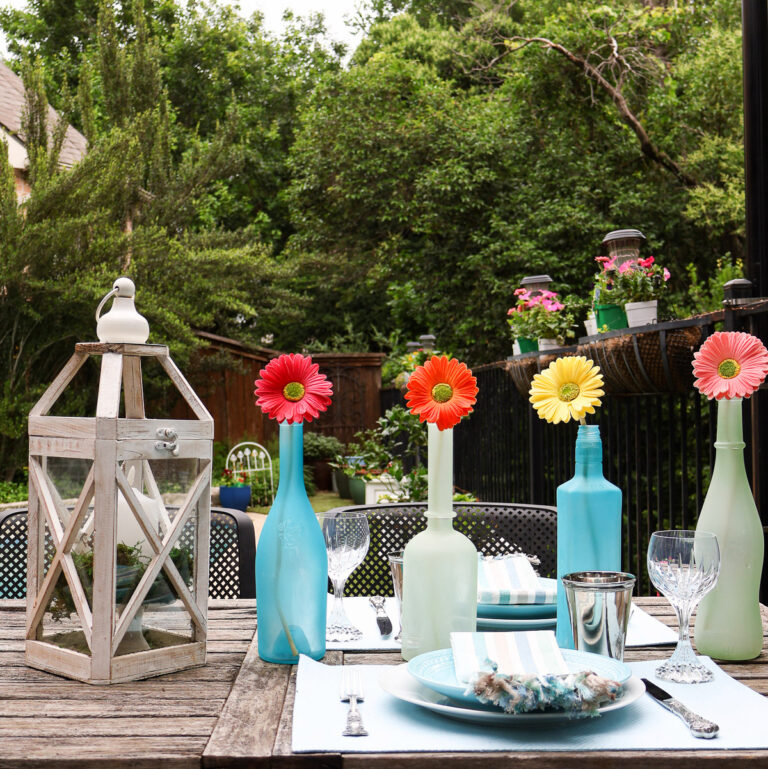 four sea glass painted bottles in aqua and sea foam with flowers on wood table for coastal tablescape
