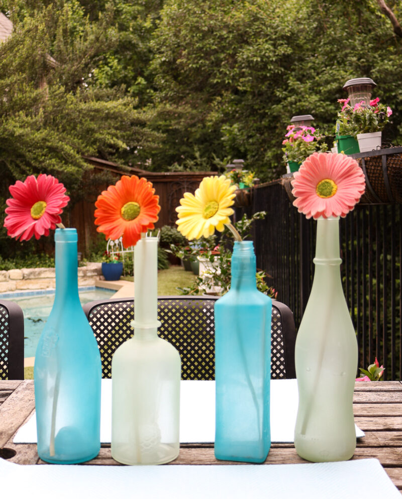 sea glass bottles filled with gerber daisies on teak table in backyard