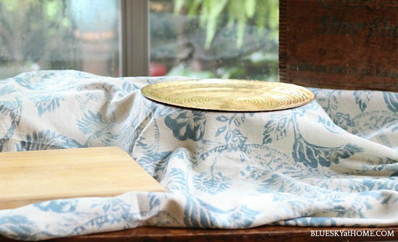 blue cloth on table with gold platter and wood cutting board