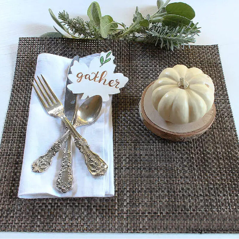 simple Thanksgiving place setting with cream-colored pumpkin, wood slice, and herbs on brown placemat