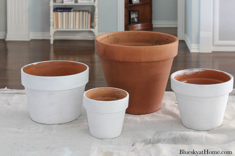 three painted white terra cotta pots and one orange terra cotta pot