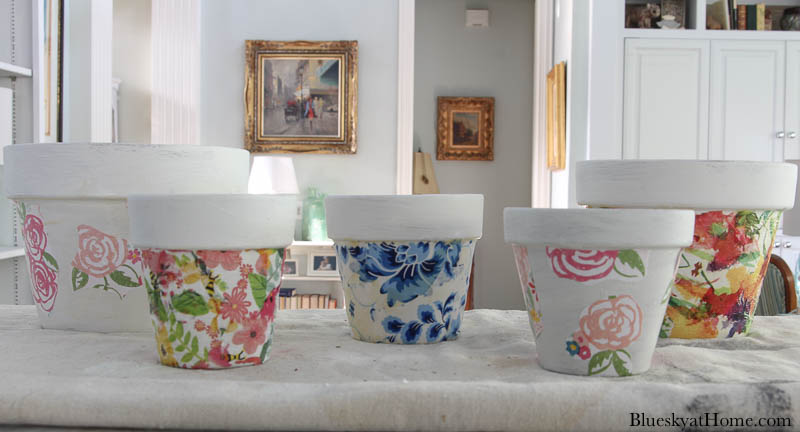 5 different decoupage terra pots in different colors of pinks, greens, and blues on kitchen counter