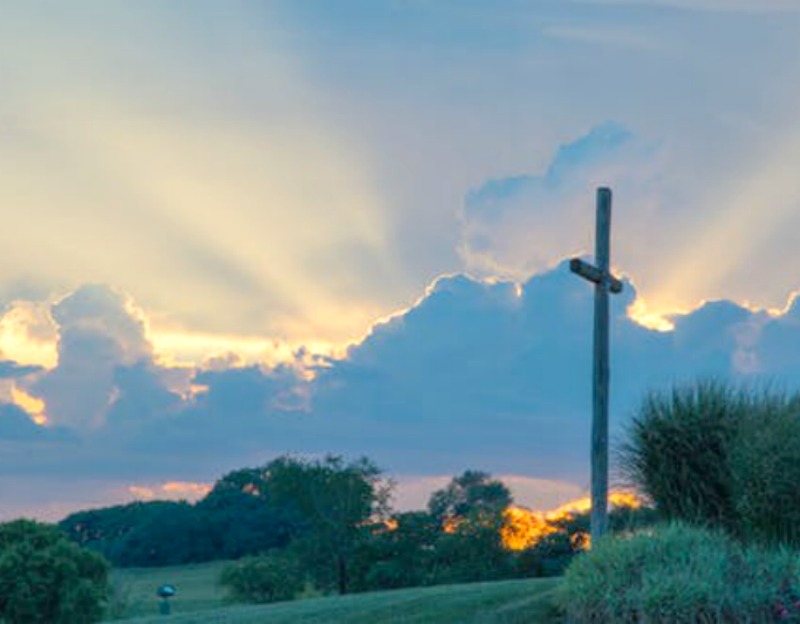 cross against blue sky with sun shining