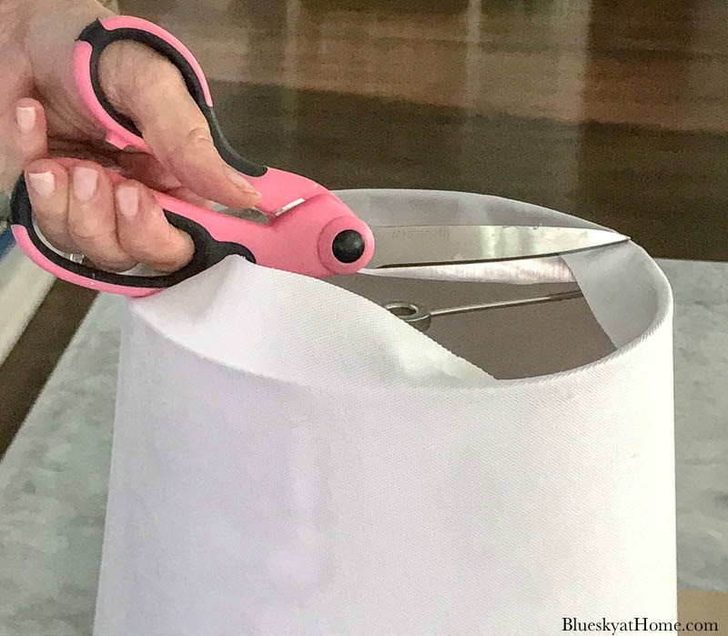 pink scissors cutting white fabric on lamp shade