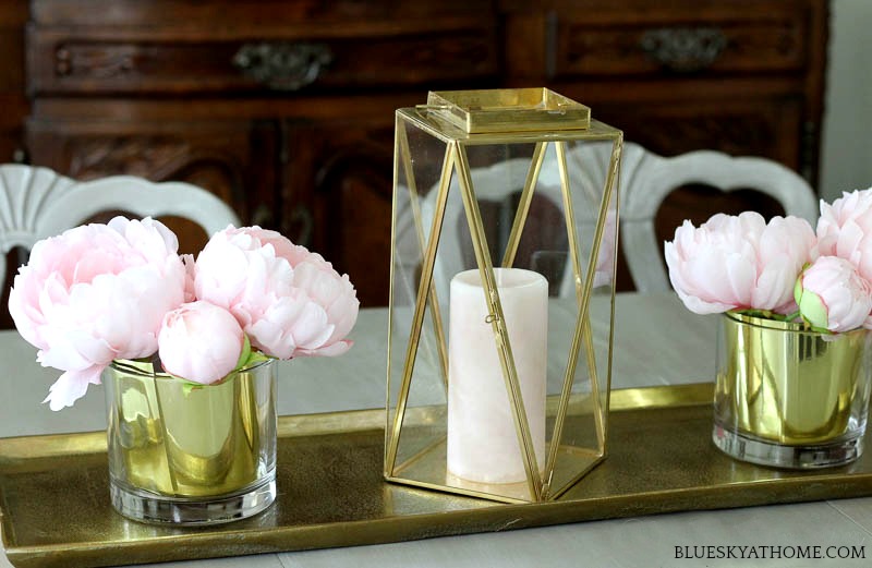 brass and glass lantern on brass tray with gold vases and pink flowers
