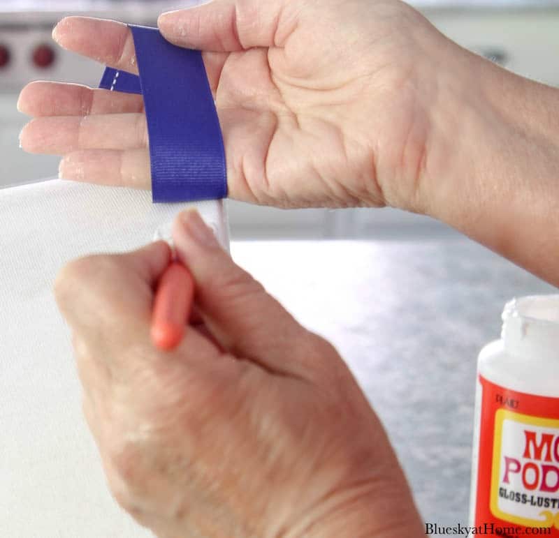 hands gluing blue ribbon on white lampshade