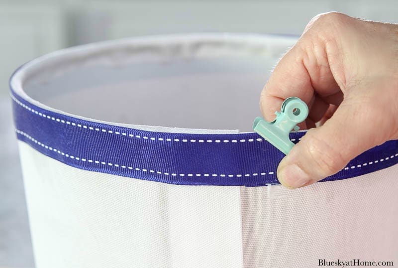 hands gluing blue ribbon on white lampshade
