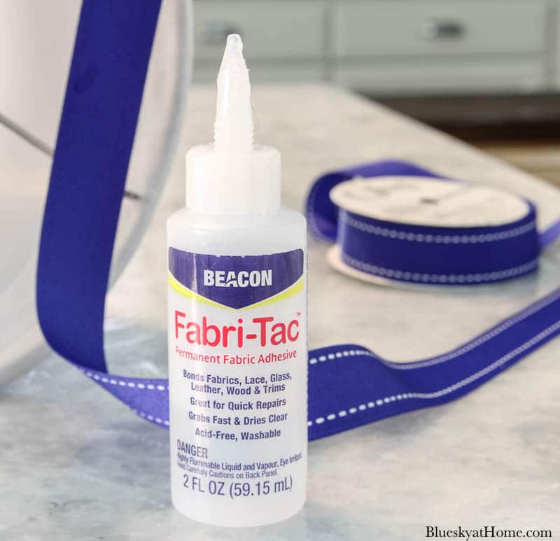 hands gluing blue ribbon on white lampshade