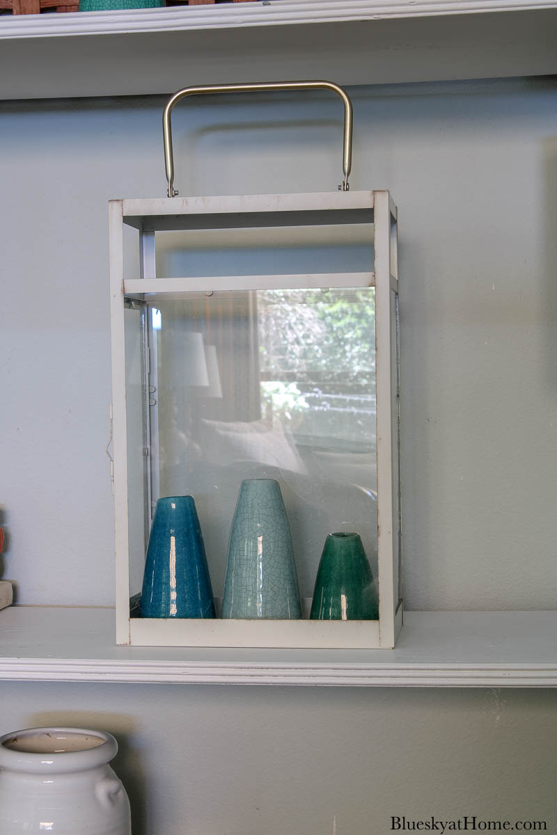 white metal and glass lantern with blue and green ceramic vases on bookcase