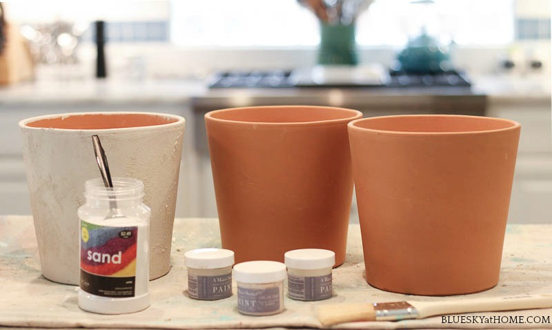 two plain orange terra cotta pots and one painted terra cotta pots with small jars of paint