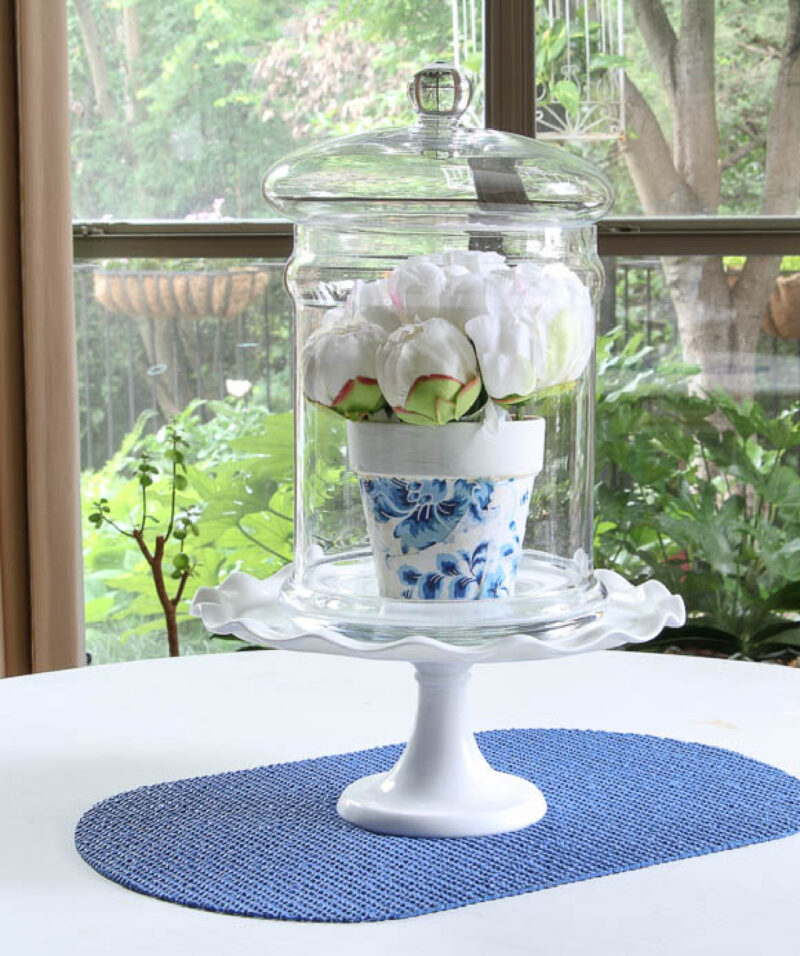 blue decoupage terra cotta pot with white flowers in a glass dome