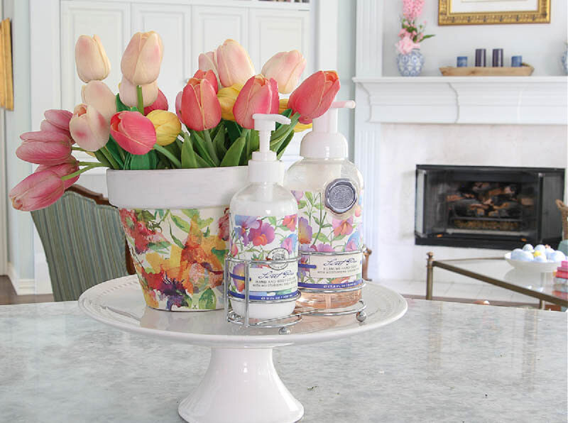 floral container of tulips on a cake stand with lotion and hand soap