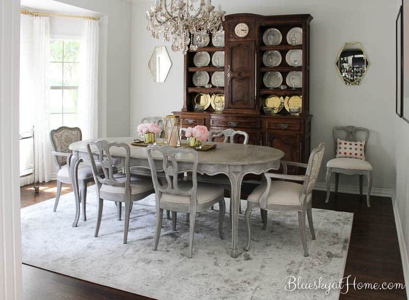 French style dining room with a grey table, rug, mirrors, and with hutch in the background