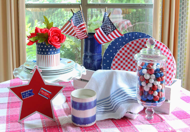 patriotic table vignette with large red star and blue and white stripe candle and blue plates with stars and red check plates with apothecary jar with red, white and blue balls