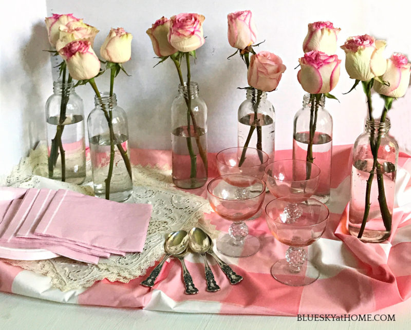 pink roses in bottles, pnk check tablecloth, pink plates, silverware, pink napkins