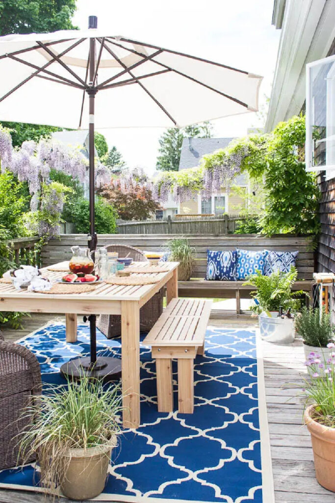 patio with blue patterned rug under dining room table and blue pattern pillows on bench