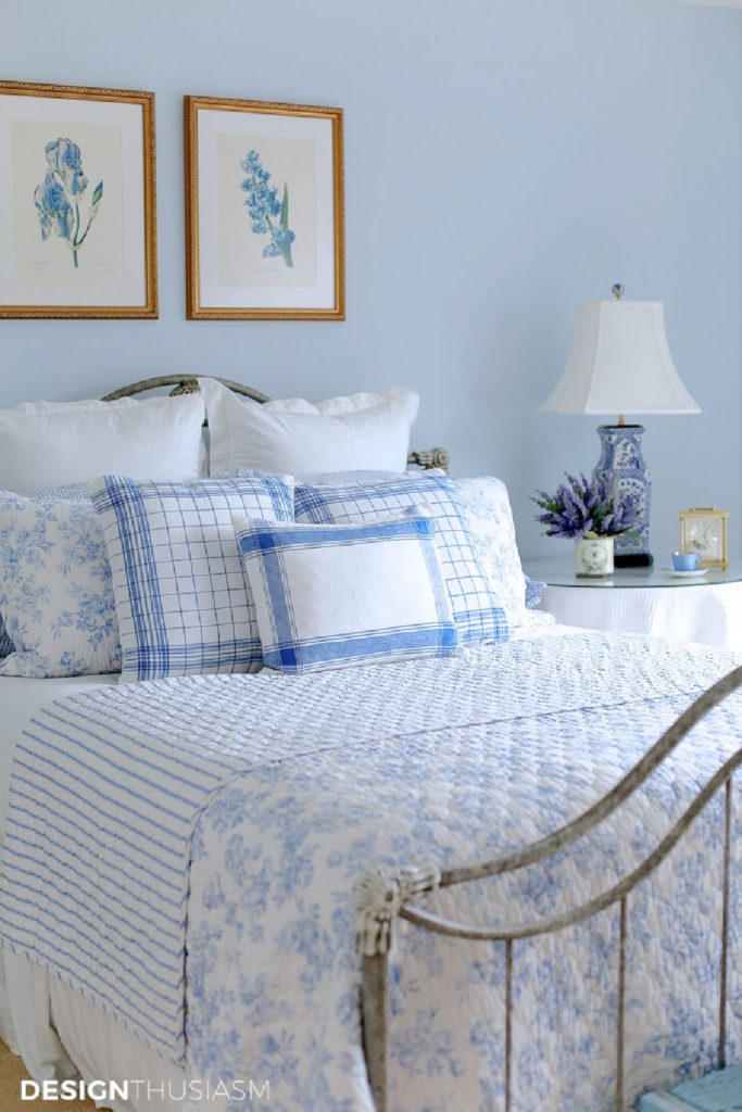 blue and white bedroom with quilt, pillows in different patterns and blue chinoiserie lamp