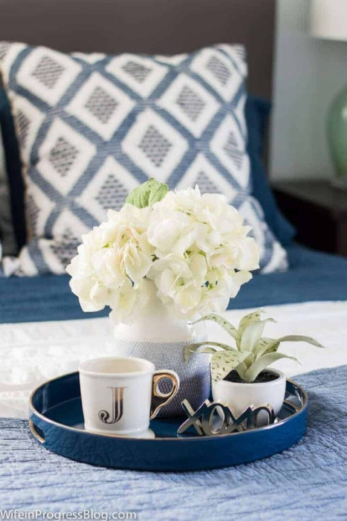 round blue tray with flowers, mug, and plant on a blue quilt