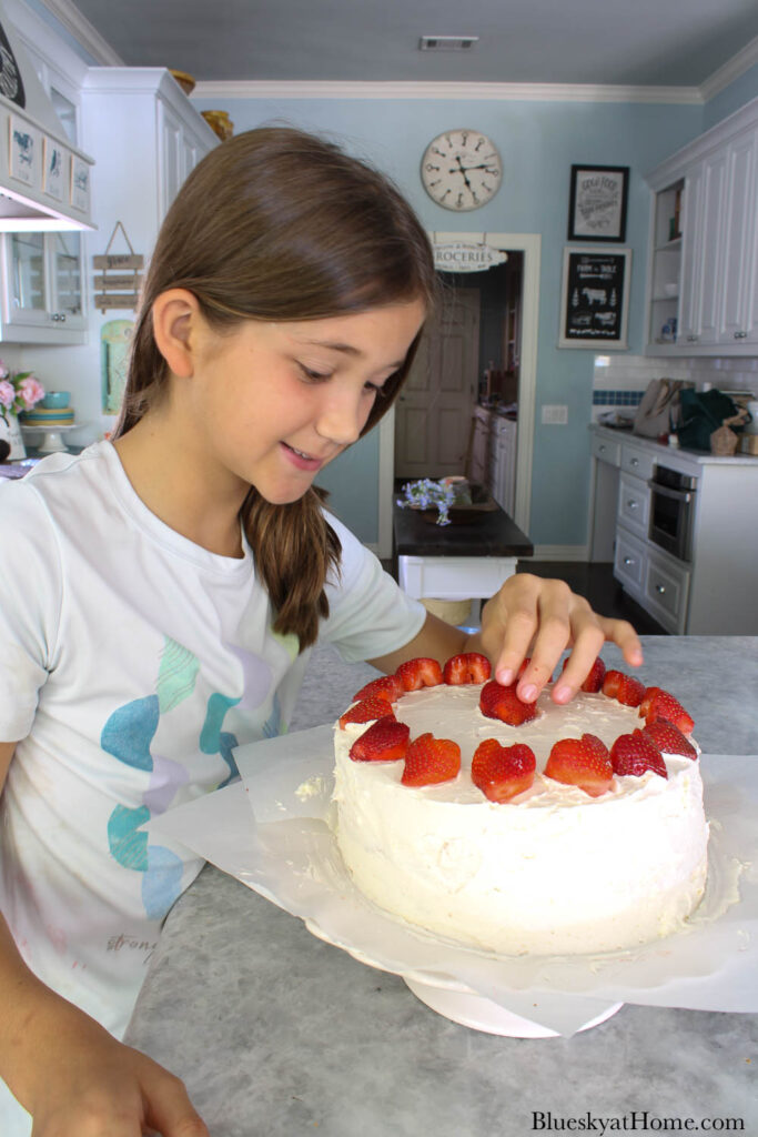 girl putting strawberry on strawberry vanilla cake