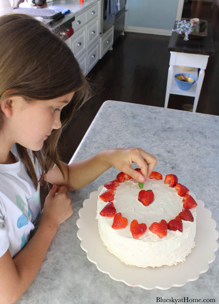 girl putting mint leaf on strawberry vanilla cake