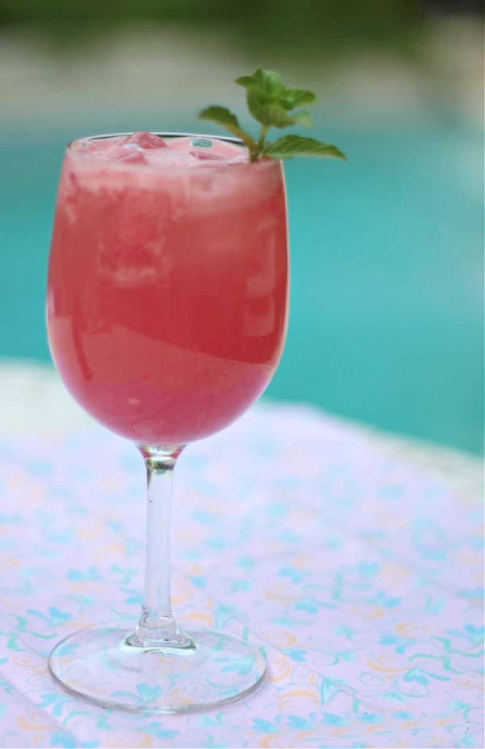red watermelon cocktail in a wine glass by the swimming pool