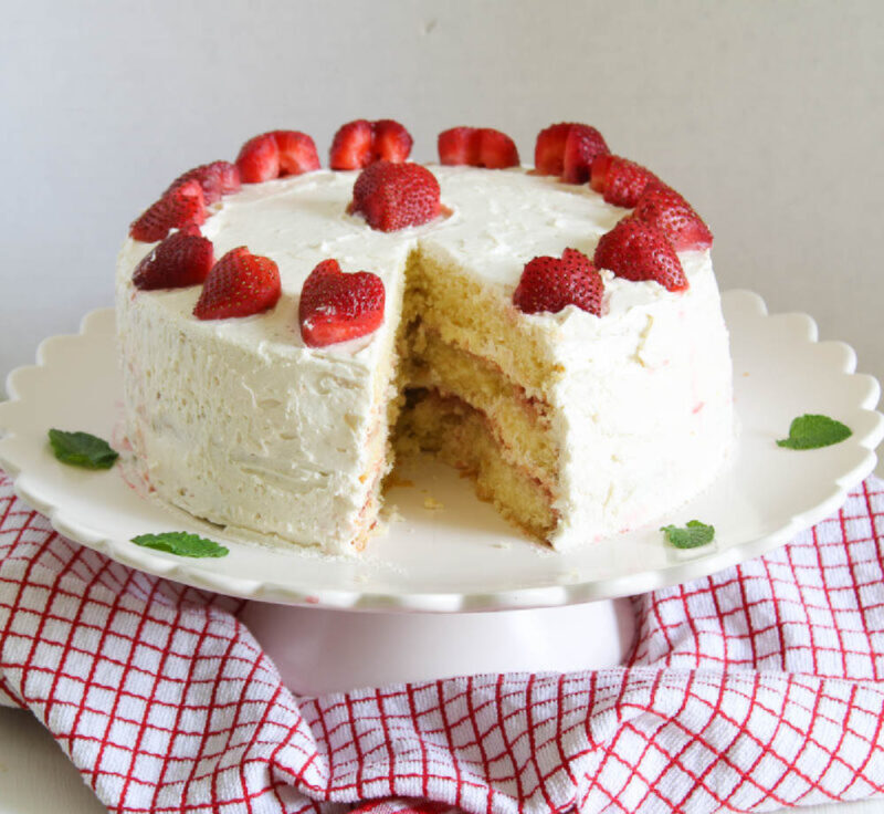 white cake with strawberries and slice cut out on cake stand