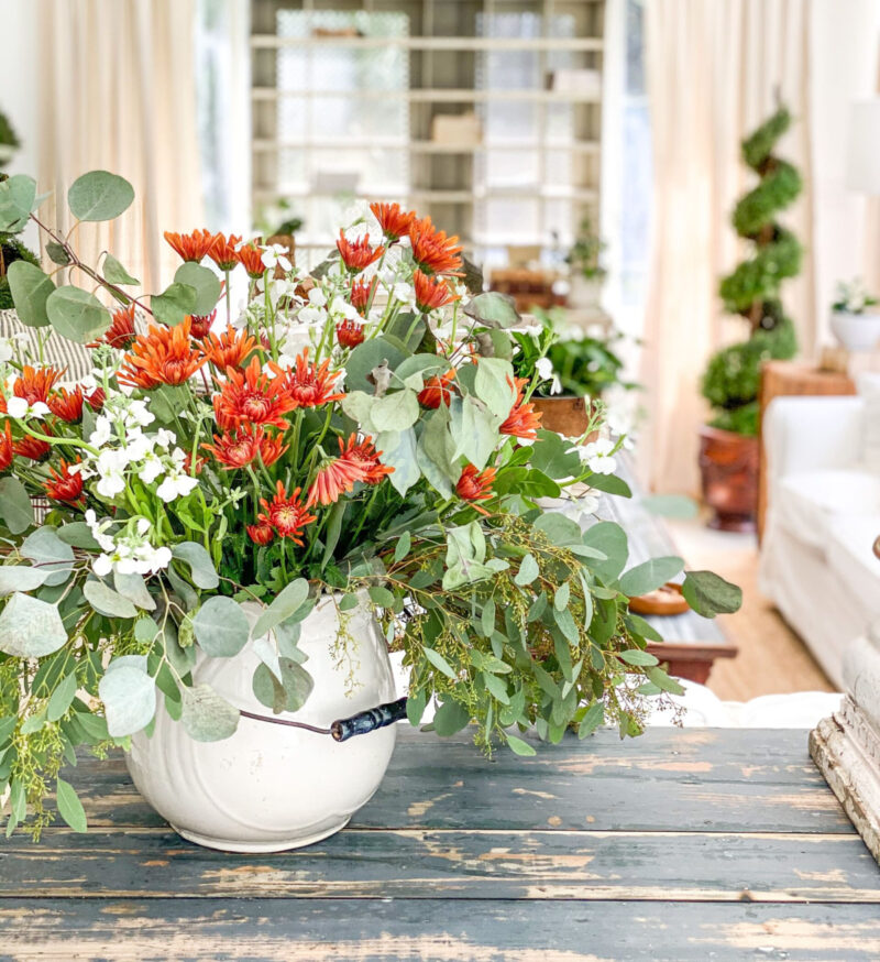 greenery with orange flowers in white pitcher with handle