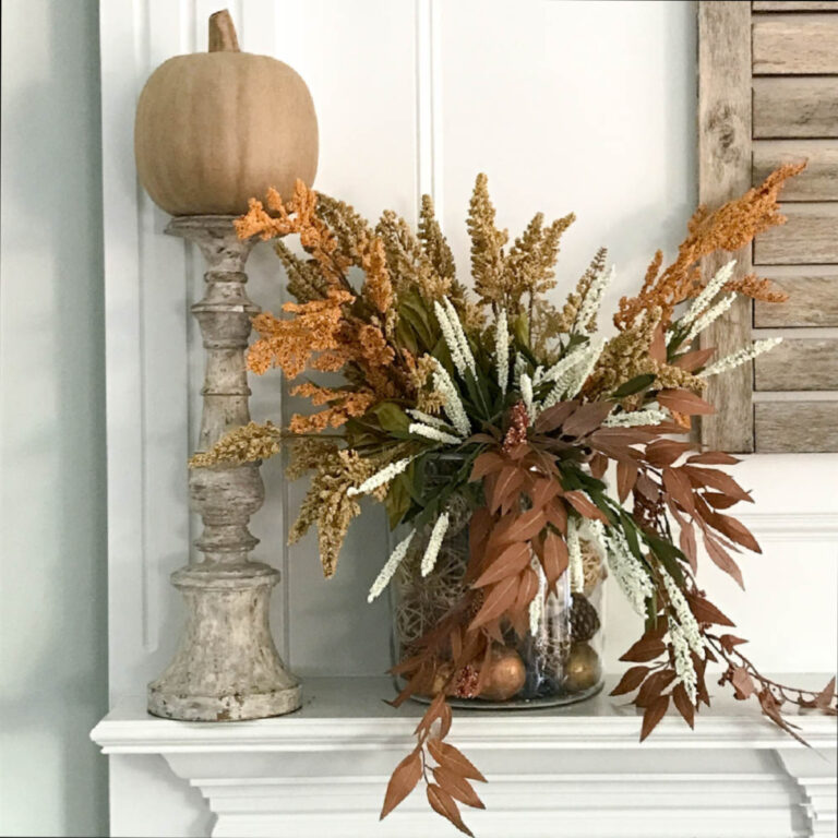 large glass jar filled with faux foliage and paper pumpkin on wood candlestick on mantel