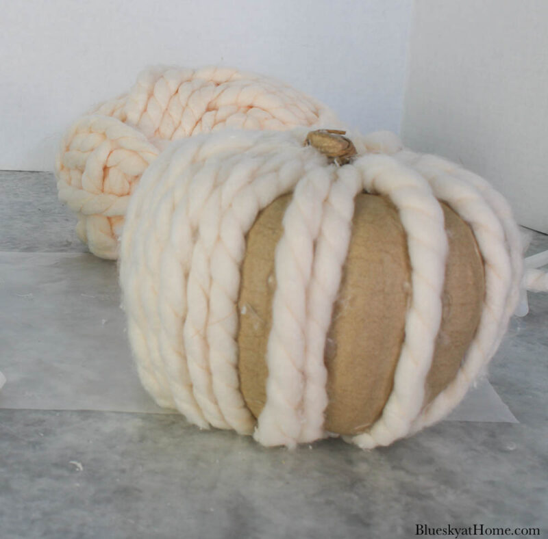 decorating a paper mache pumpkin with cream-colored yarn