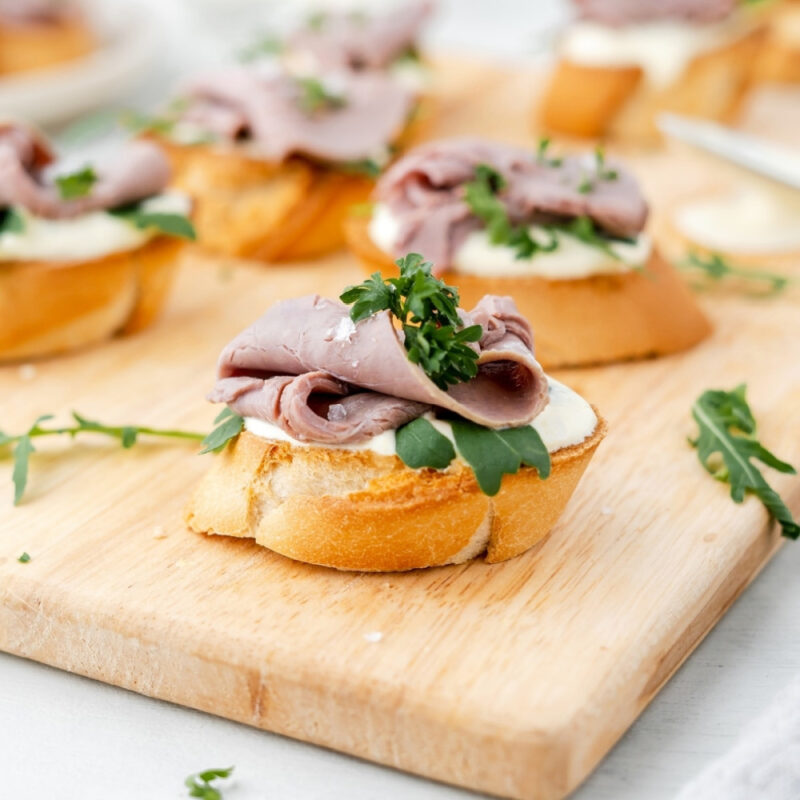 roast beef crostini on wood cutting board