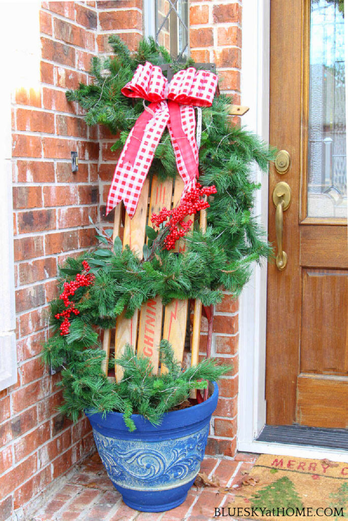 front door decorated with Christmas garland on sleigh