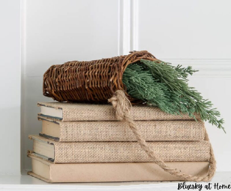greenery in woven basket on stack of burlap covered books