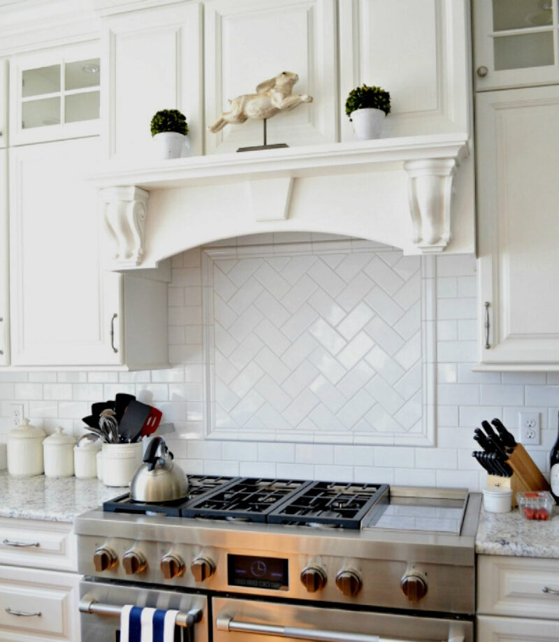 white tile stove backsplash and white hood as focal point