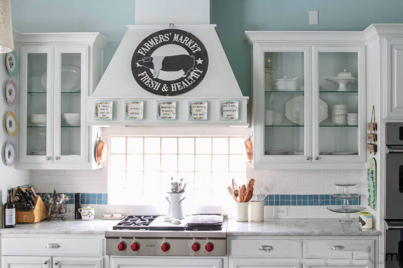 white kitchen with central focal point of stove hood between glass front cabinets