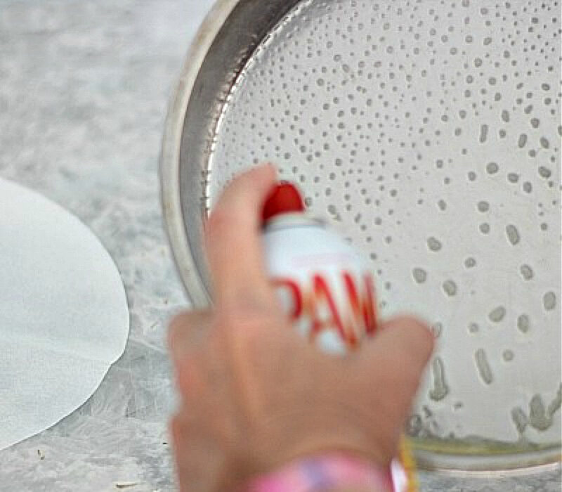 spraying parchment paper round in cake pan