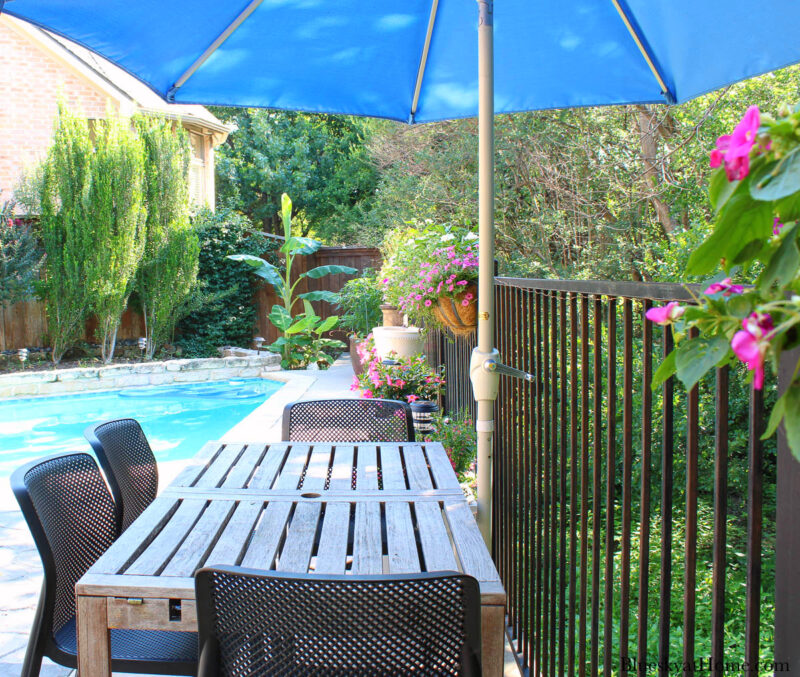teak patio table with blue umbrella against fence