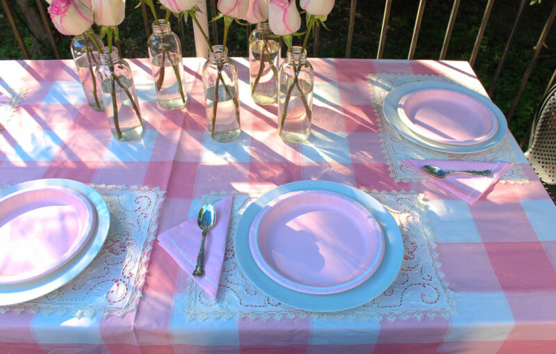 glass bottles and pale pink flowers with silverware on patio table