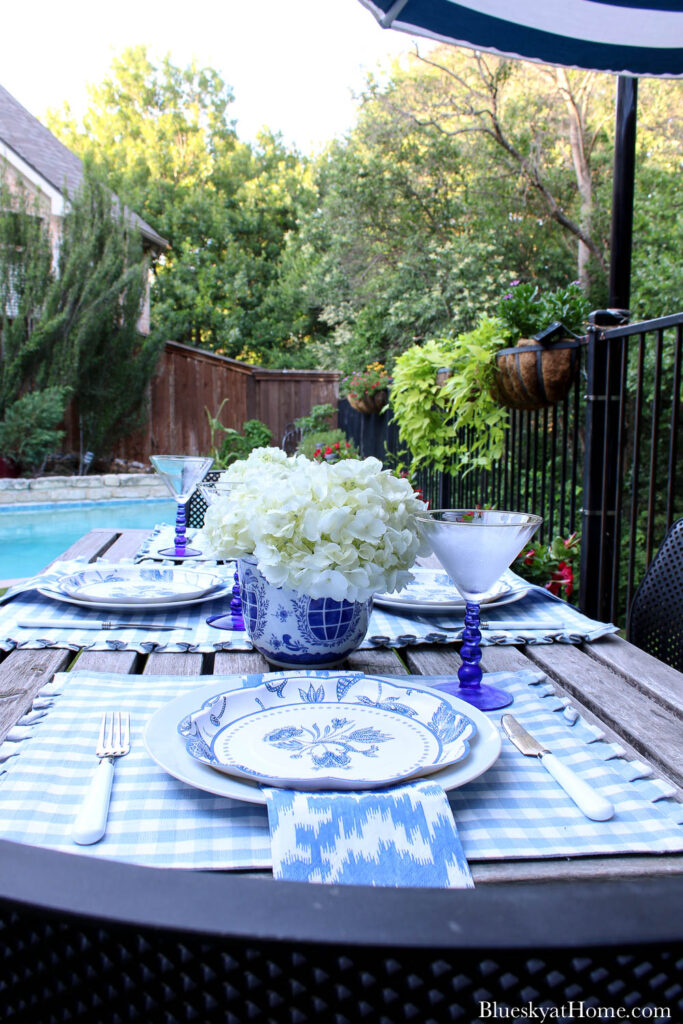 outdoor summer table decor with blue placemats, dishes, napkins, and glasses 