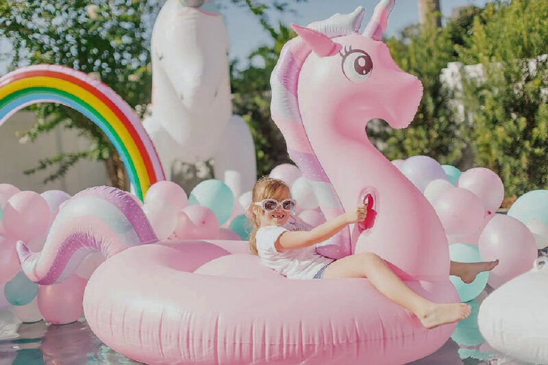 little girl in a unicorn swim float in swimming pool