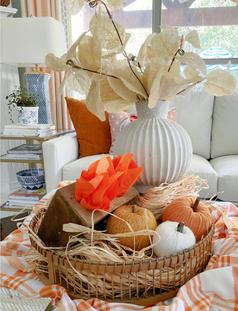 fall vignette with white round vase, yarn pumpkins, and bright orange tissue paper on coffee table
