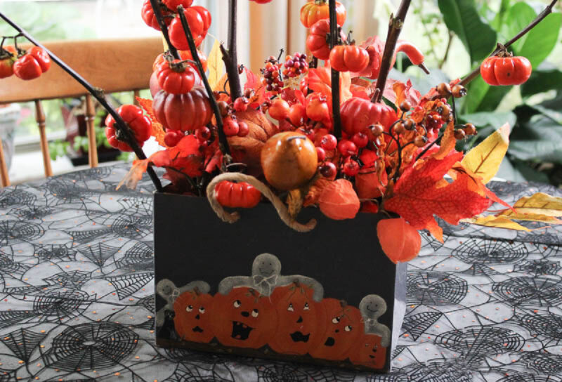 container with orange fall decor on spider table cloth