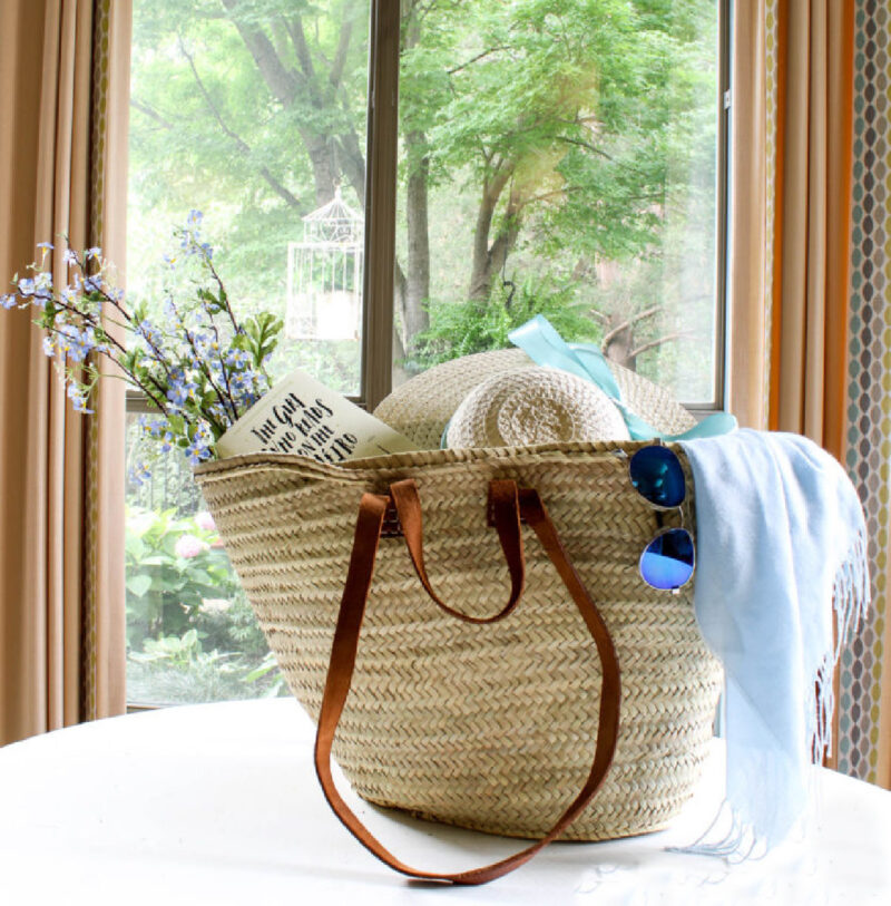 idea for decorating basket French woven tote basket bag with leather handles, straw hat, blue shawl, blue gun glasses and book