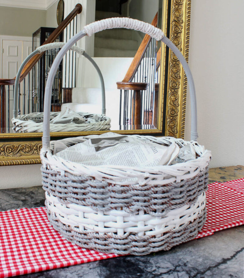 grey and white painted woven basket with handle stuffed with newspaper