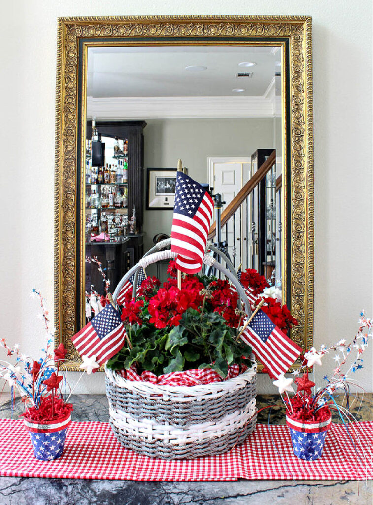 idea for decorating basket grey and white painted woven basket with handle and red geraniums and American flags on red check runner and stars and stripes pots 
